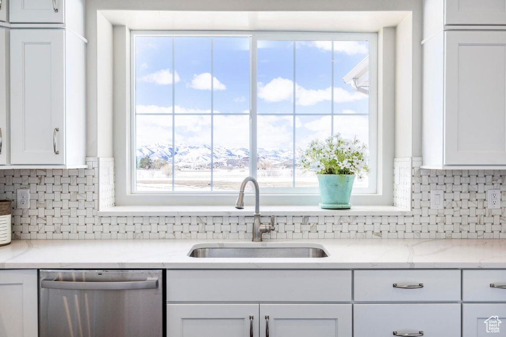 Kitchen with stainless steel dishwasher, a sink, white cabinets, and backsplash