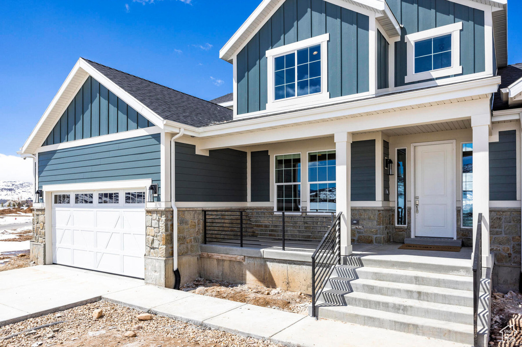 View of front of home featuring board and batten siding, stone siding, a porch, and driveway