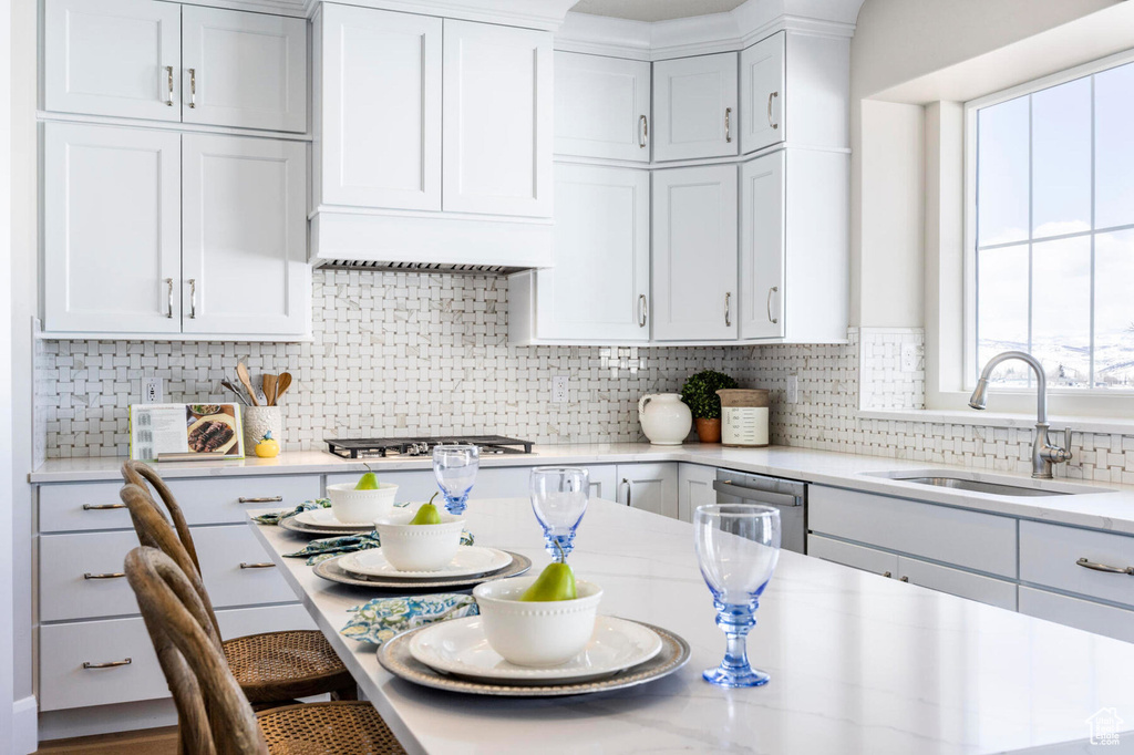 Kitchen featuring a sink, a kitchen bar, backsplash, white cabinetry, and stainless steel appliances