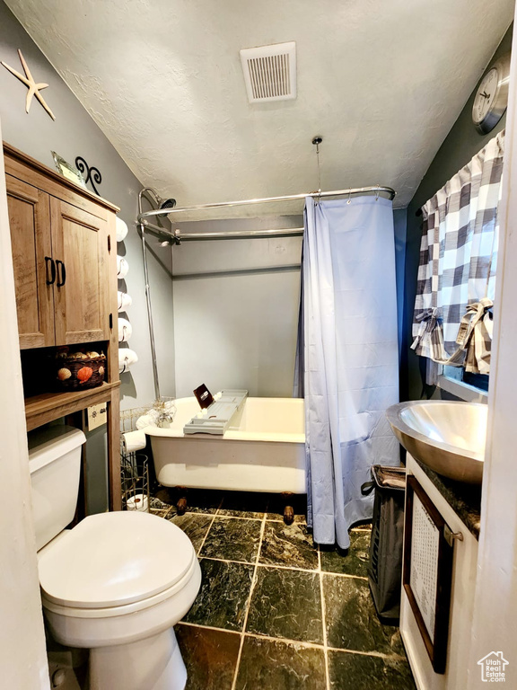 Bathroom featuring toilet, stone finish floors, shower / bath combination with curtain, and vanity