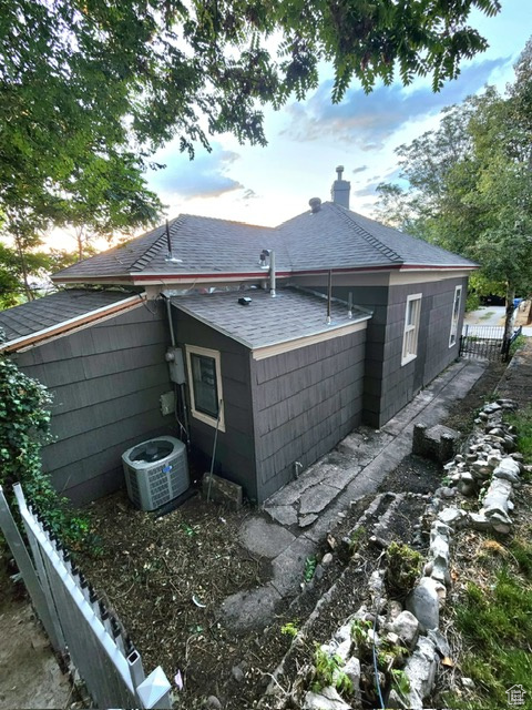 Back of house at dusk with a shingled roof, central AC, and a chimney