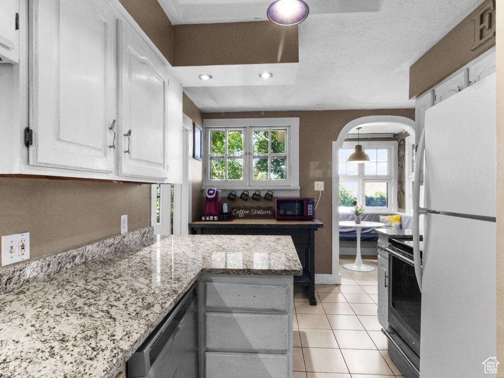 Kitchen with stainless steel appliances, white cabinetry, arched walkways, light tile patterned flooring, and light stone counters