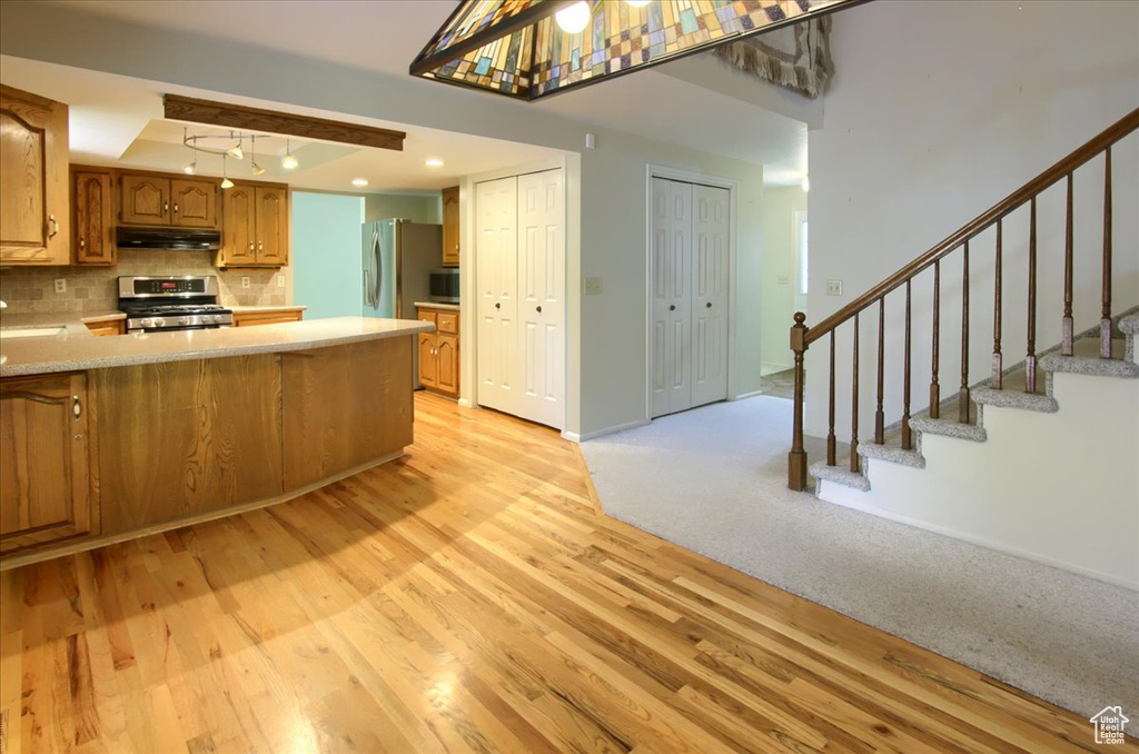 Kitchen featuring appliances with stainless steel finishes, light wood-type flooring, under cabinet range hood, light countertops, and decorative backsplash