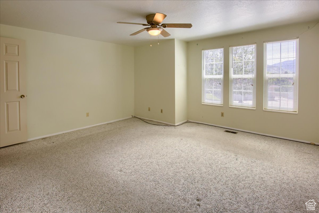 Carpeted spare room featuring ceiling fan and baseboards