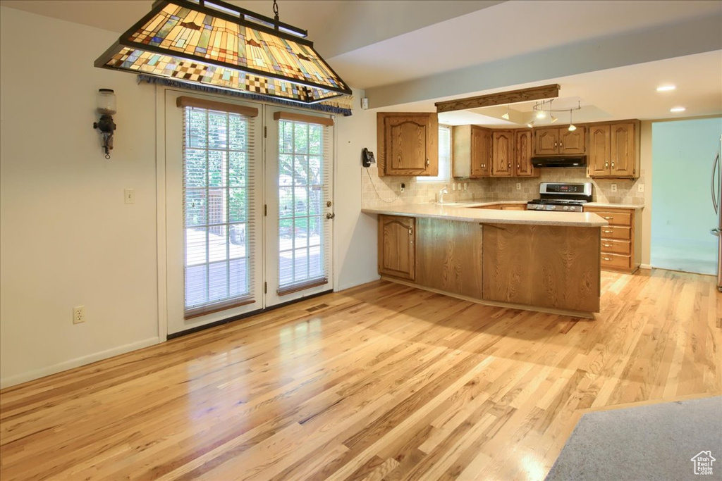 Kitchen with stainless steel appliances, under cabinet range hood, light wood finished floors, light countertops, and a peninsula