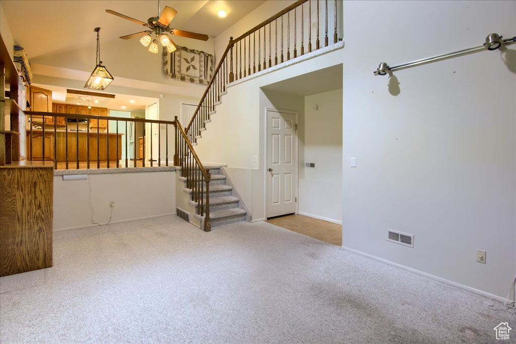 Unfurnished living room with stairs, ceiling fan, carpet floors, a towering ceiling, and baseboards