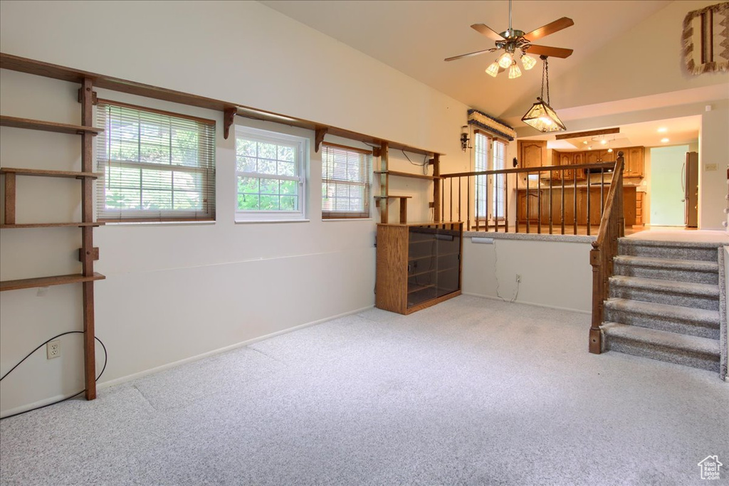 Carpeted empty room featuring a ceiling fan, stairs, lofted ceiling, and baseboards