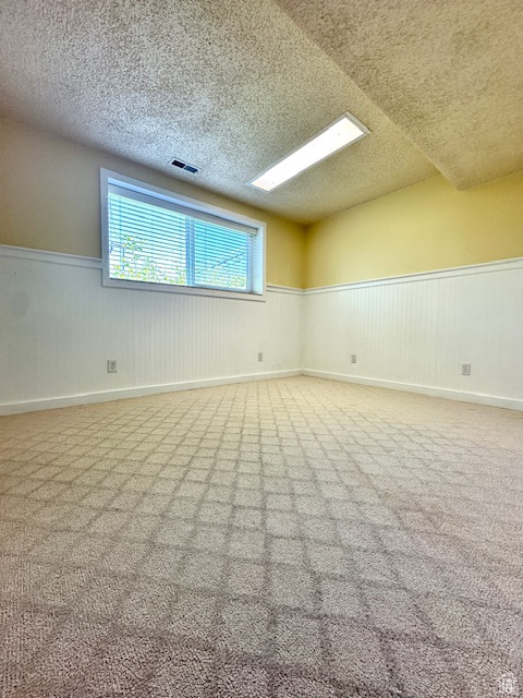 Spare room with wainscoting, a textured ceiling, and carpet floors