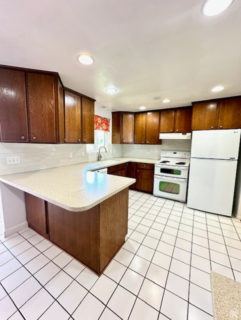 Kitchen featuring white appliances, under cabinet range hood, light countertops, a peninsula, and tasteful backsplash