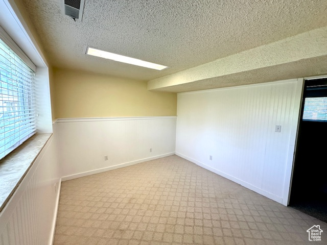 Carpeted spare room with a textured ceiling and a wainscoted wall