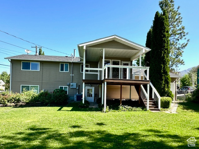 Rear view of house featuring stairs, a lawn, and a wooden deck