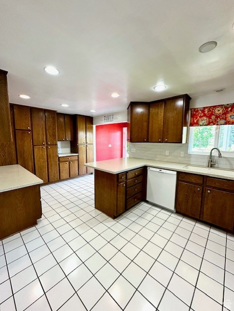 Kitchen featuring dishwasher, a sink, a peninsula, light countertops, and decorative backsplash