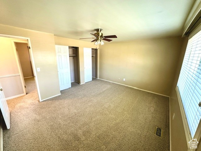 Unfurnished bedroom featuring carpet floors, baseboards, ceiling fan, and multiple closets