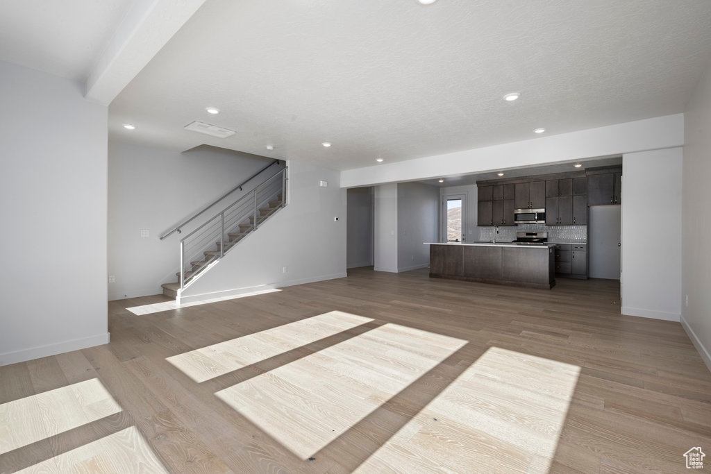 Unfurnished living room with stairway, baseboards, light wood-type flooring, recessed lighting, and a sink