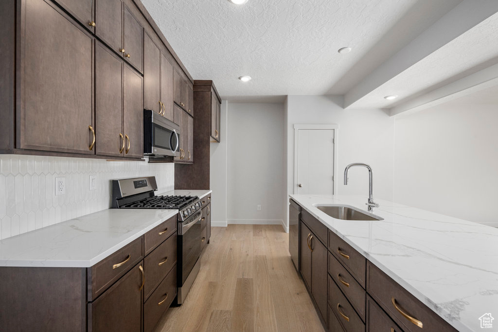 Kitchen with appliances with stainless steel finishes, a sink, light wood-style floors, dark brown cabinets, and a textured ceiling