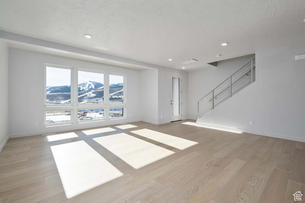 Unfurnished living room featuring baseboards, recessed lighting, light wood-style floors, stairs, and a textured ceiling