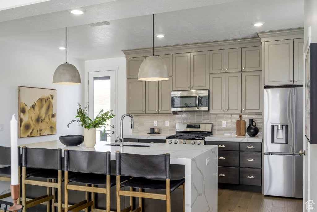 Kitchen with stainless steel appliances, a sink, tasteful backsplash, wood finished floors, and a breakfast bar area