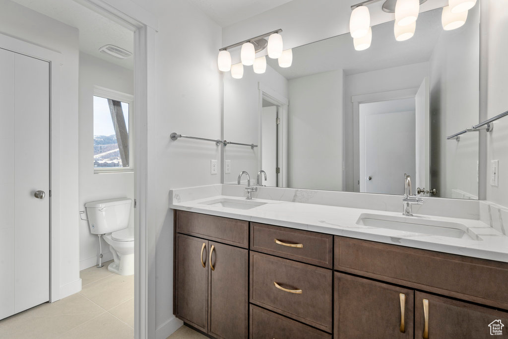 Full bathroom featuring double vanity, toilet, baseboards, and tile patterned flooring