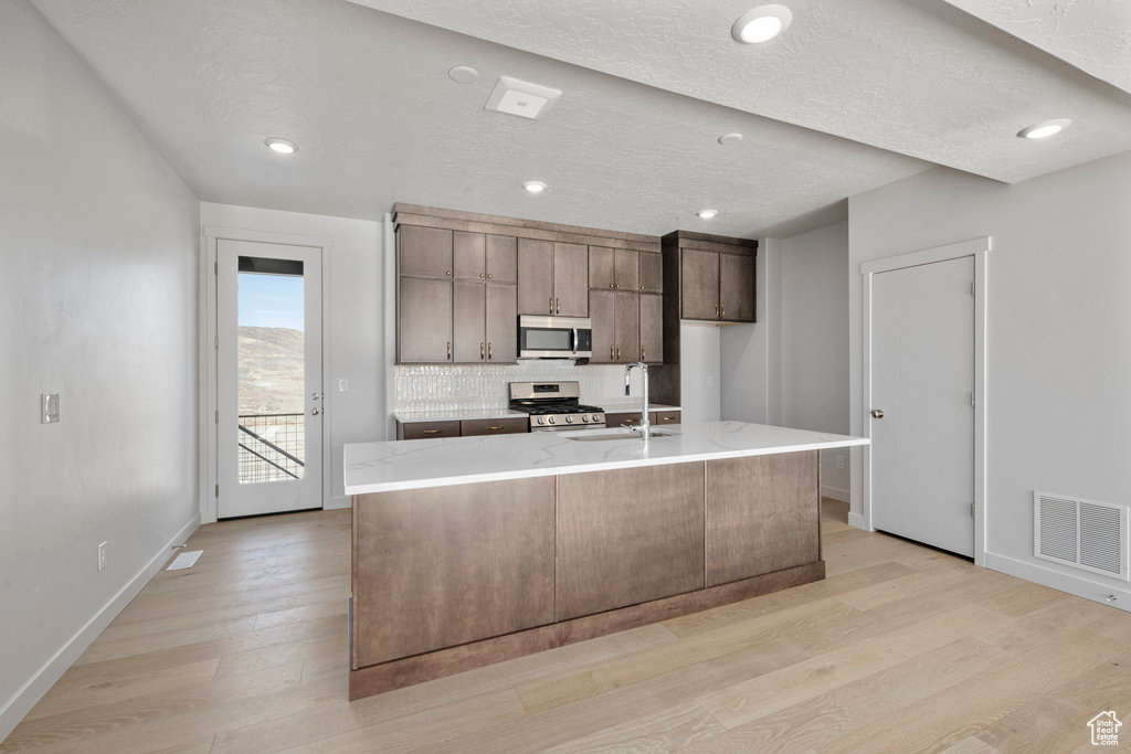 Kitchen with appliances with stainless steel finishes, a sink, light wood-style flooring, baseboards, and recessed lighting