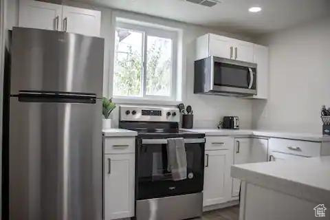 Kitchen featuring appliances with stainless steel finishes, light countertops, white cabinets, and wood finished floors