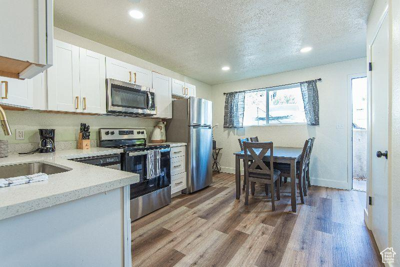 Kitchen with appliances with stainless steel finishes, a sink, a textured ceiling, light wood-style floors, and white cabinetry