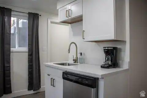 Kitchen featuring stainless steel dishwasher, a sink, light countertops, white cabinets, and baseboards