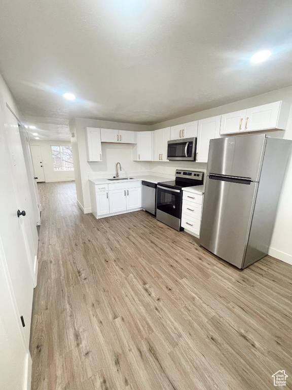 Kitchen featuring stainless steel appliances, a sink, light wood-style flooring, light countertops, and white cabinetry