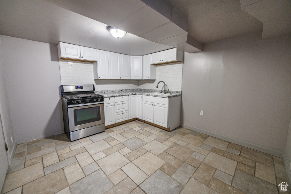 Kitchen featuring stainless steel range with gas stovetop, a sink, backsplash, light stone counters, and stone tile floors