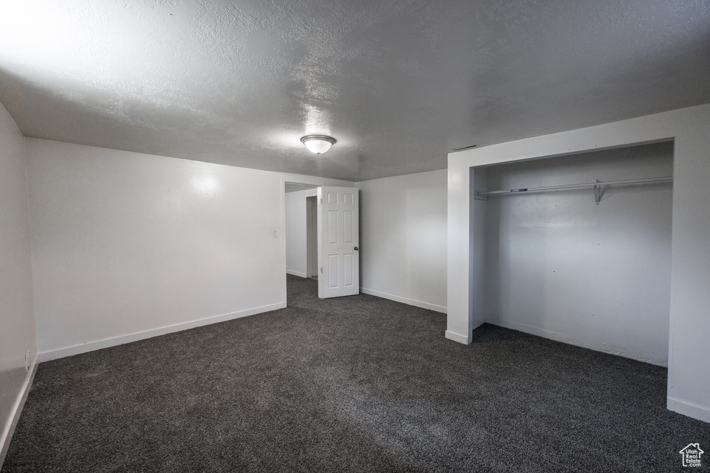 Unfurnished bedroom featuring dark colored carpet, baseboards, a textured ceiling, and a closet