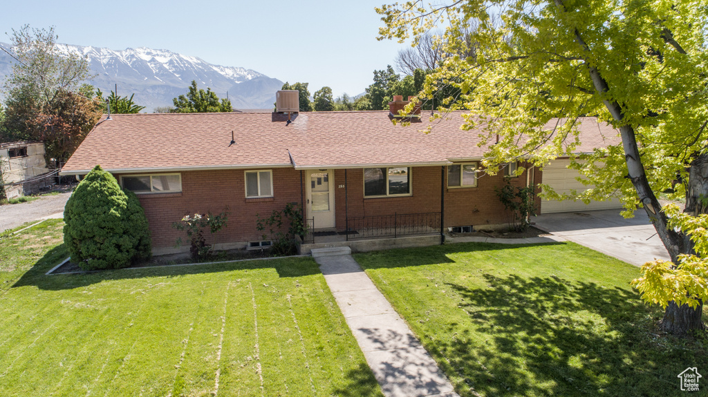 Ranch-style house featuring brick siding, a front lawn, concrete driveway, a mountain view, and roof with shingles