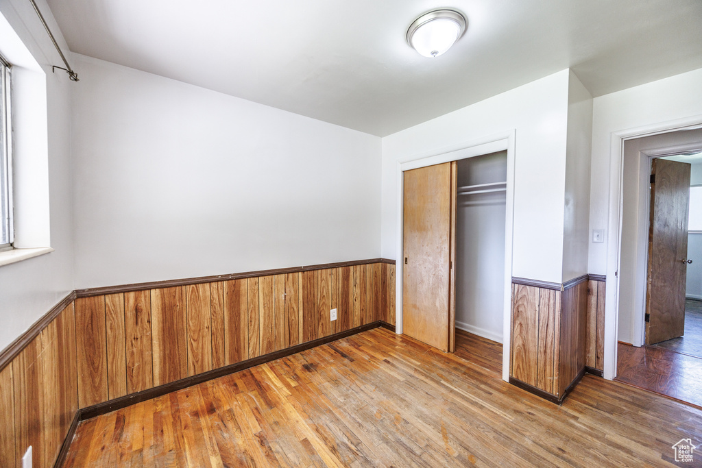 Unfurnished bedroom featuring a wainscoted wall, wood-type flooring, a closet, and wood walls