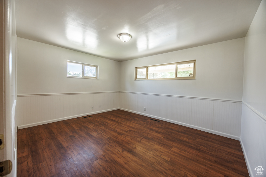 Unfurnished room with dark wood finished floors, wainscoting, and plenty of natural light