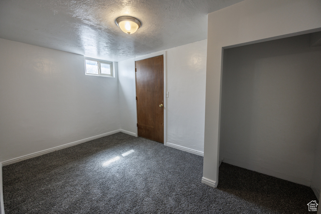 Unfurnished bedroom with dark colored carpet, a textured ceiling, and baseboards