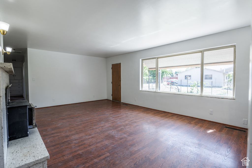 Unfurnished living room featuring dark wood-style flooring and a wood stove