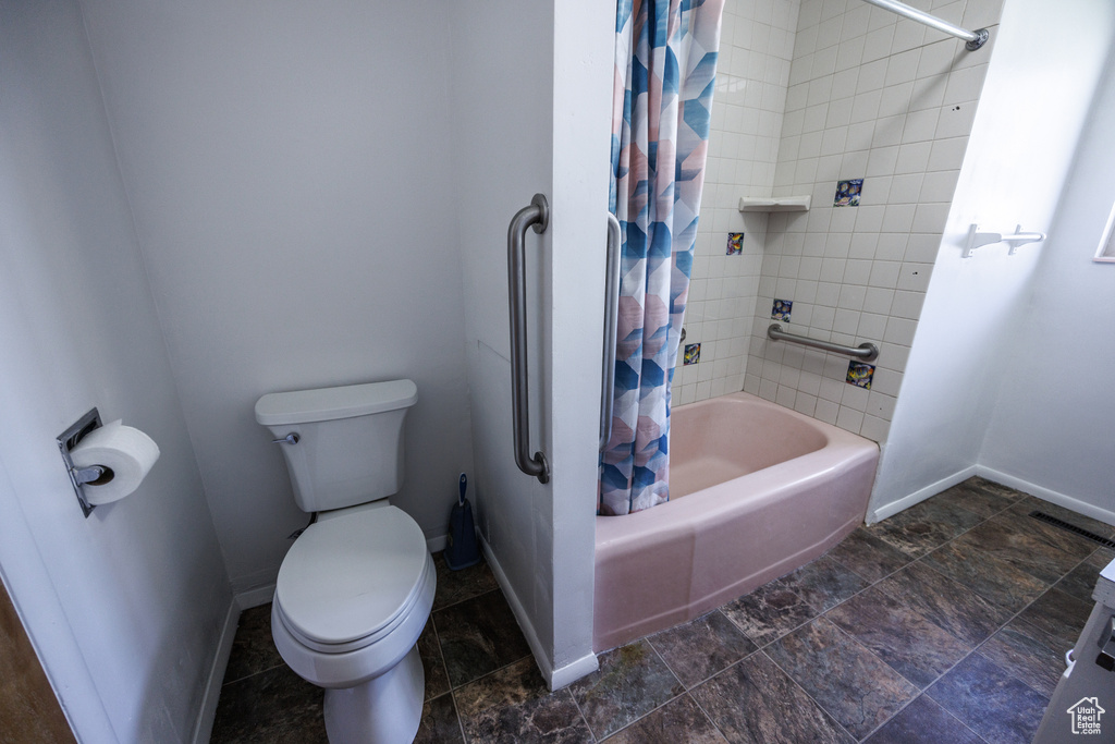 Bathroom with shower / bath combo, baseboards, toilet, and stone finish floors