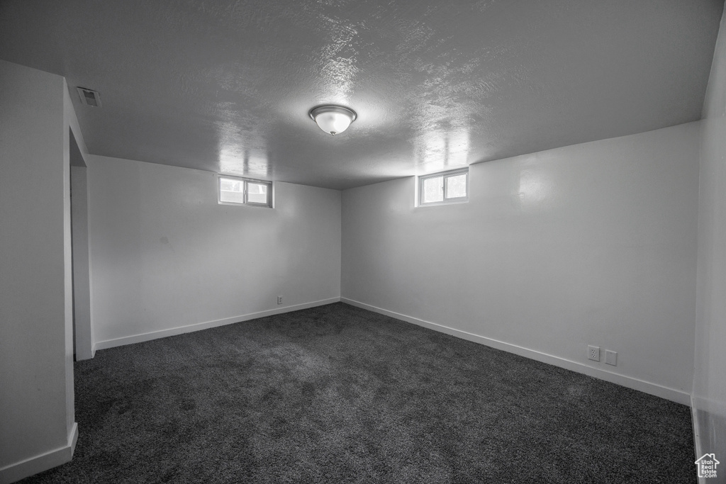 Basement with a textured ceiling, dark carpet, baseboards, and plenty of natural light