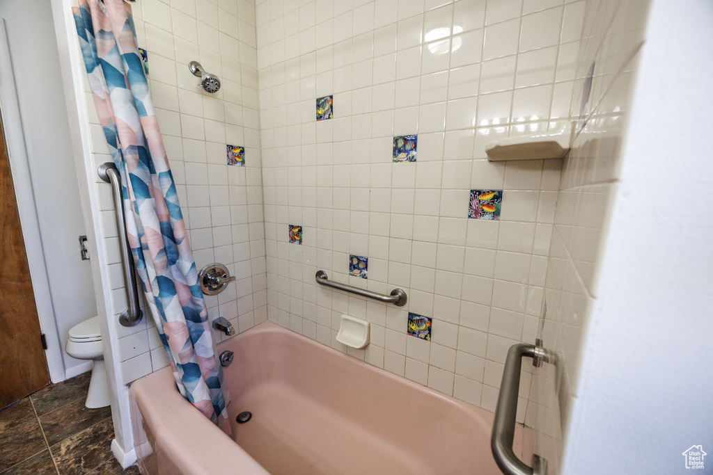 Bathroom with shower / bath combo, toilet, and stone finish flooring
