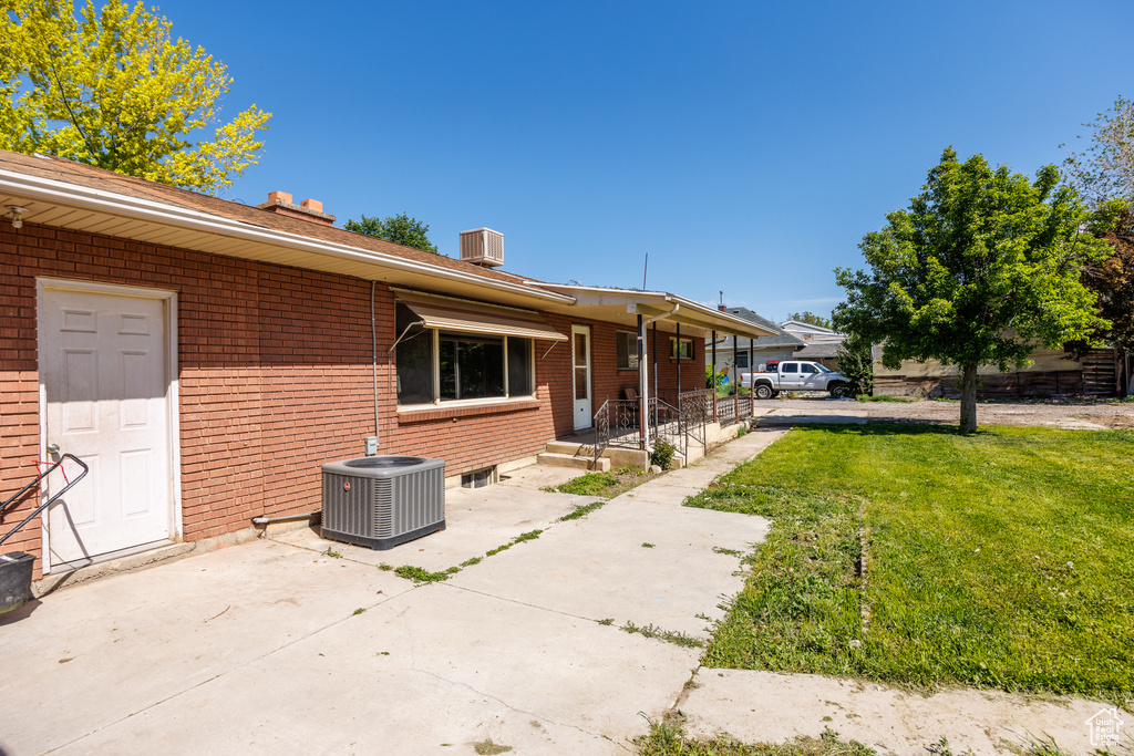 View of side of home with central AC, brick siding, a lawn, and a chimney