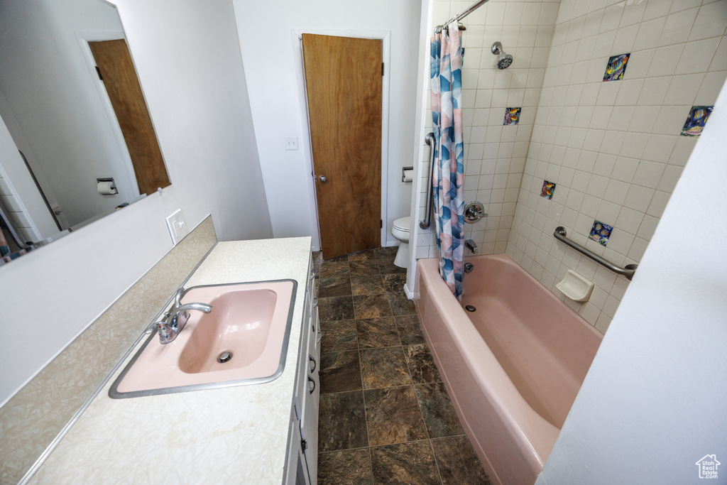 Full bathroom with toilet, stone finish floors, vanity, and shower / bath combo with shower curtain