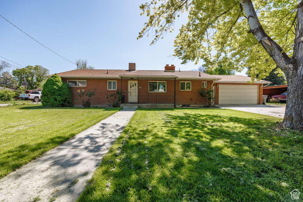 Ranch-style home featuring a chimney, a garage, brick siding, and driveway