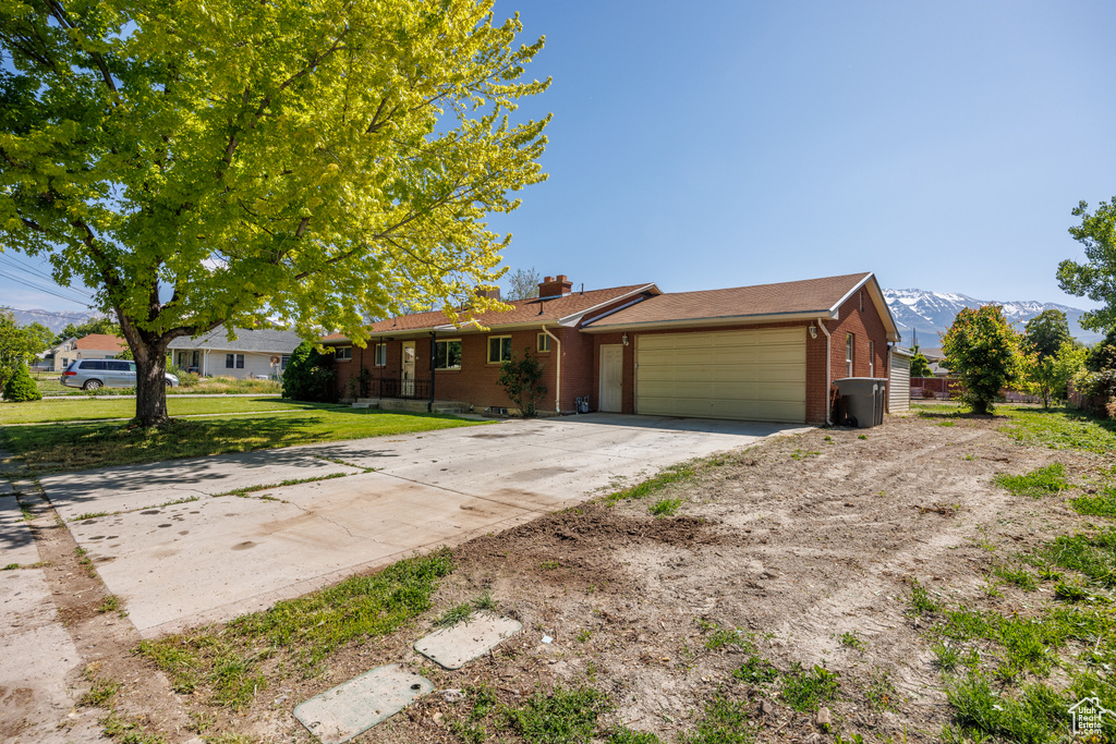 Ranch-style home featuring brick siding, a garage, driveway, a chimney, and a mountain view