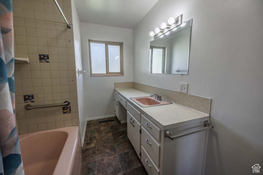 Bathroom with vanity, stone finish floors, shower / bath combo with shower curtain, and baseboards