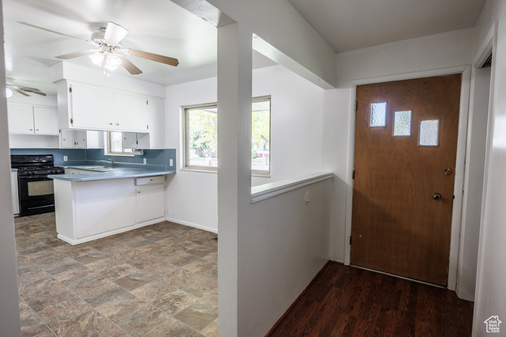 Kitchen featuring black gas stove, a sink, white cabinetry, a ceiling fan, and a peninsula