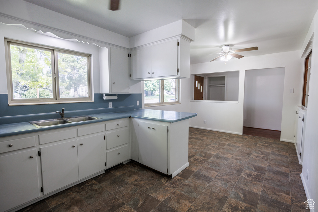 Kitchen with a sink, ceiling fan, stone finish floors, white cabinets, and a peninsula