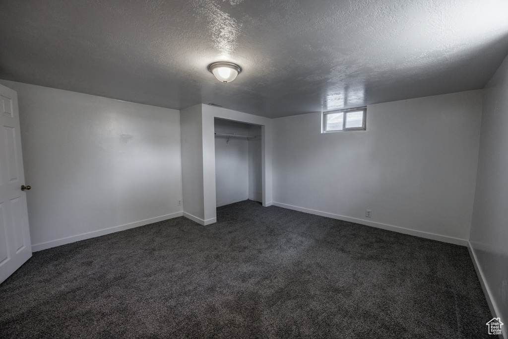 Unfurnished bedroom featuring a textured ceiling, dark colored carpet, baseboards, and a closet