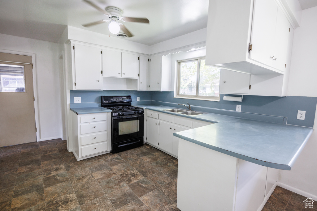 Kitchen with black gas stove, a sink, a peninsula, and white cabinets