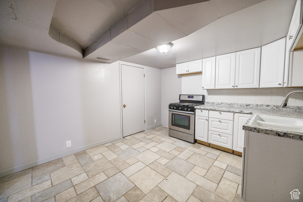 Kitchen featuring gas stove, a sink, white cabinetry, and baseboards