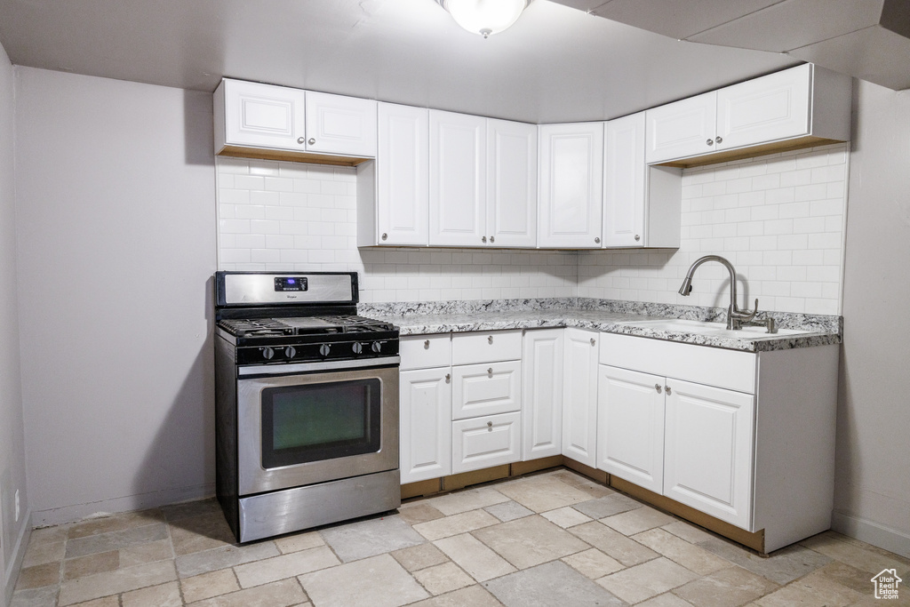 Kitchen featuring stainless steel gas range oven, a sink, stone tile floors, and backsplash