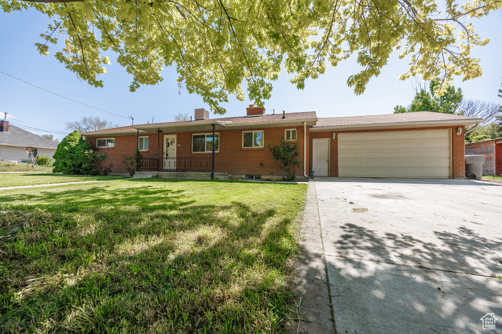 Ranch-style home featuring brick siding, a garage, concrete driveway, a front yard, and a chimney