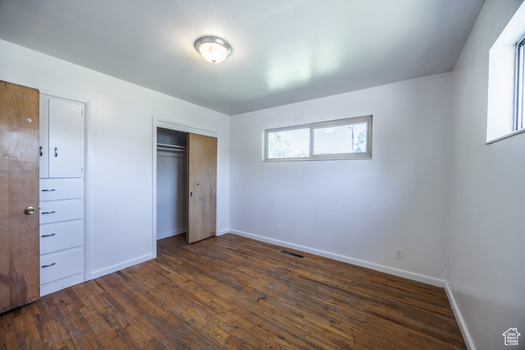 Unfurnished bedroom featuring baseboards, dark wood-style flooring, and a closet